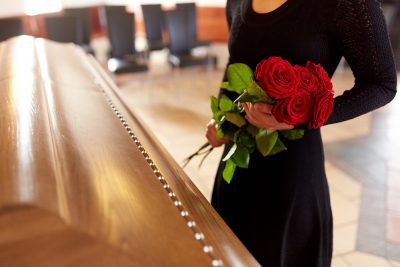 woman with red roses and coffin at funeral in church